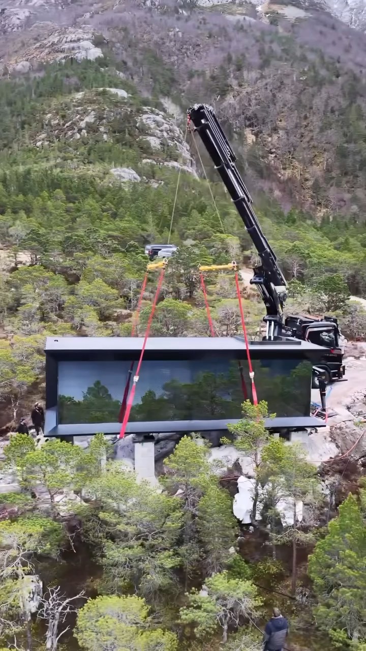 Flat-roof FLAT cabin being placed by crane on a rocky wooded site