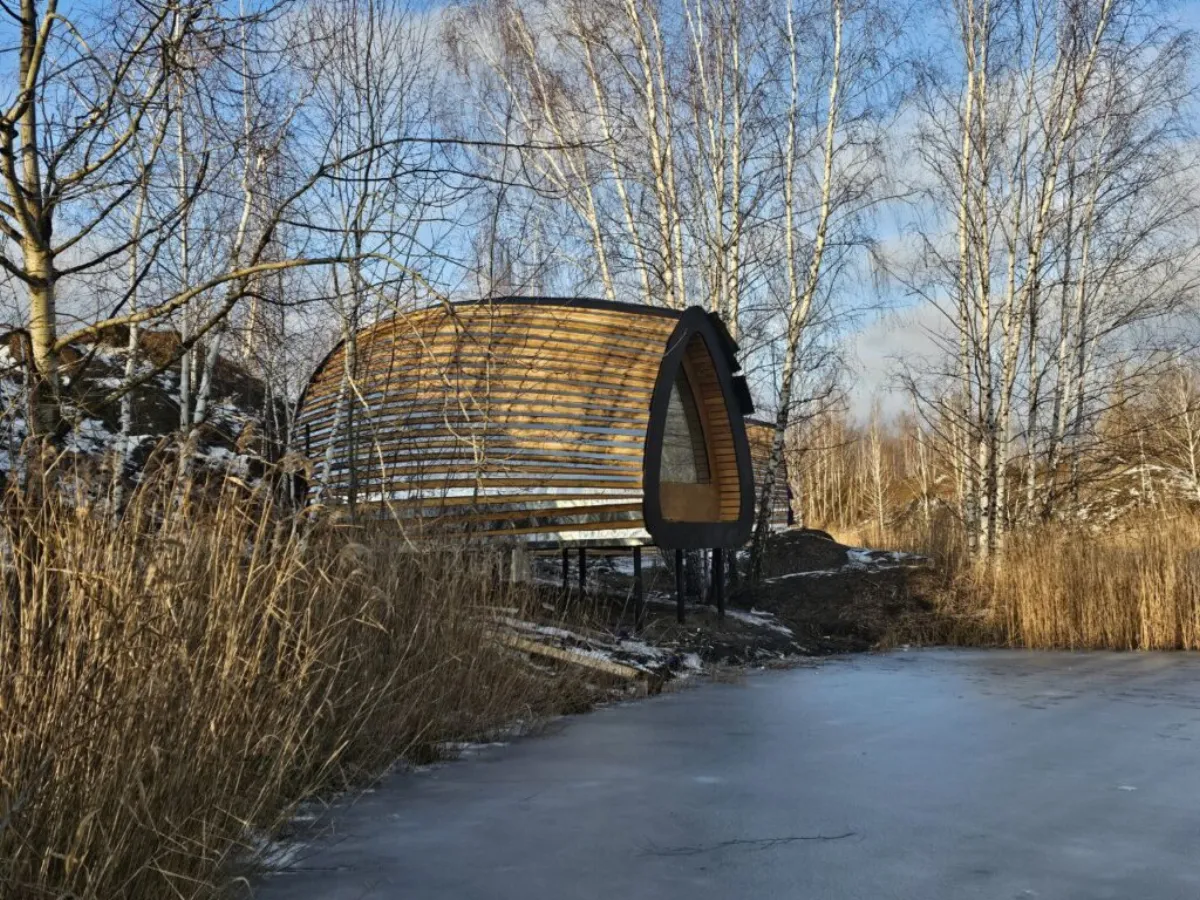 Built HIZ cabin with a curved timber exterior beside a frozen lake